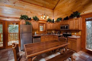 A wooden cabin interior with a kitchen, dining table, and benches. - Bear's Bliss Luxury Cabin with Pool & Theater (Sevier County)
