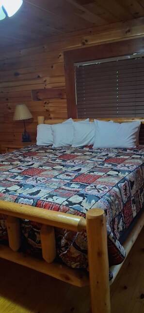 A wooden cabin-style room with a bed, a window with blinds, and a lamp on a nightstand. - Bear's Bliss Luxury Cabin with Pool & Theater (Sevier County)