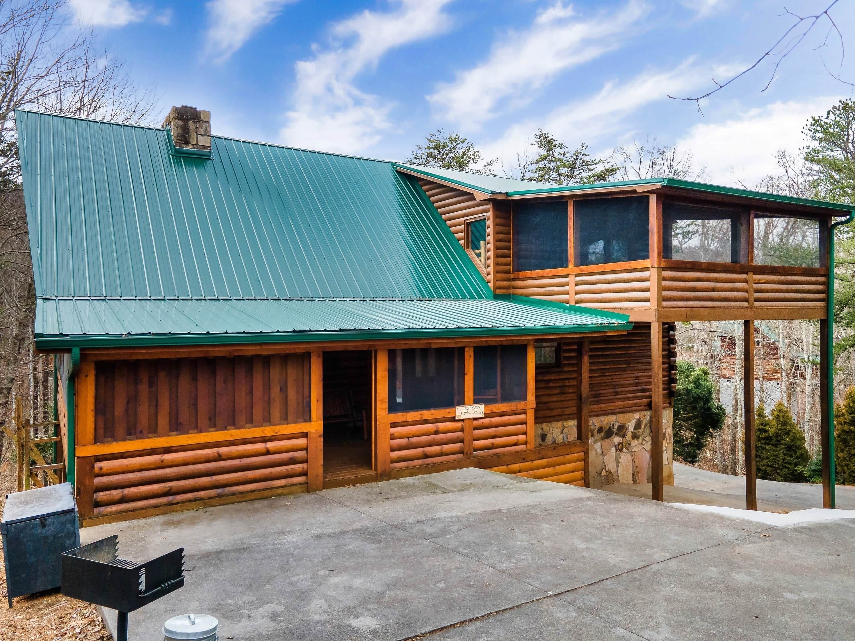 A log cabin with a green metal roof, a stone foundation, and a concrete patio.