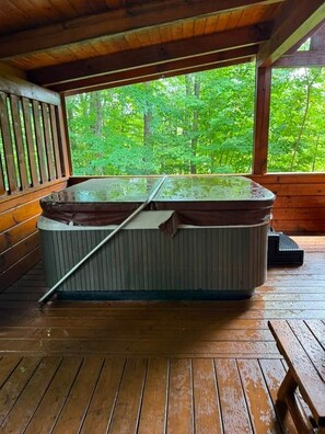 A hot tub in a wooden cabin with a view of a forest.