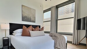 Een hotelkamer met een groot bed, een nachtkastje, een lamp en uitzicht op gebouwen.