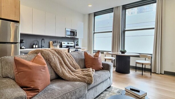 Een moderne woonkamer met een grijze bank, een salontafel, en een eethoek met een ronde tafel en stoelen.