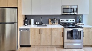 Een moderne keuken met roestvrijstalen apparatuur, houten kastjes en een zwarte achterwand.