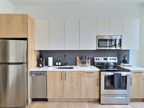 Eine moderne Küche mit Edelstahlgeräten, Holzschränken und einer schwarzen Spritzschutzwand.