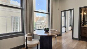 Een modern interieur met een ronde tafel en twee stoelen, grote ramen met gordijnen en een uitzicht op gebouwen.