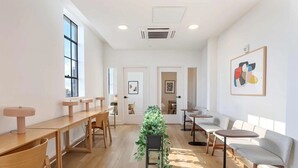Een ruime kamer met houten tafels en stoelen, een plant in het midden en kunstwerken aan de muren.