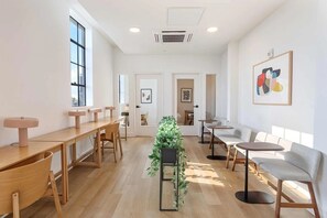 Ein geräumiger Raum mit Holztischen und -stühlen, einer zentral platzierten Pflanze und Kunstwerken an den Wänden.