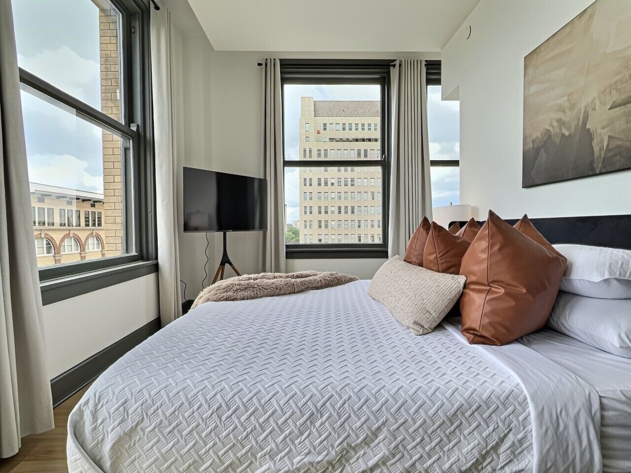 Habitación de hotel con una cama grande, una televisión de pantalla plana y vistas a un paisaje urbano desde la ventana.
