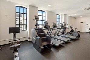 Une salle de sport équipée de tapis de course, de vélos d’appartement et d’un appareil d’aviron.