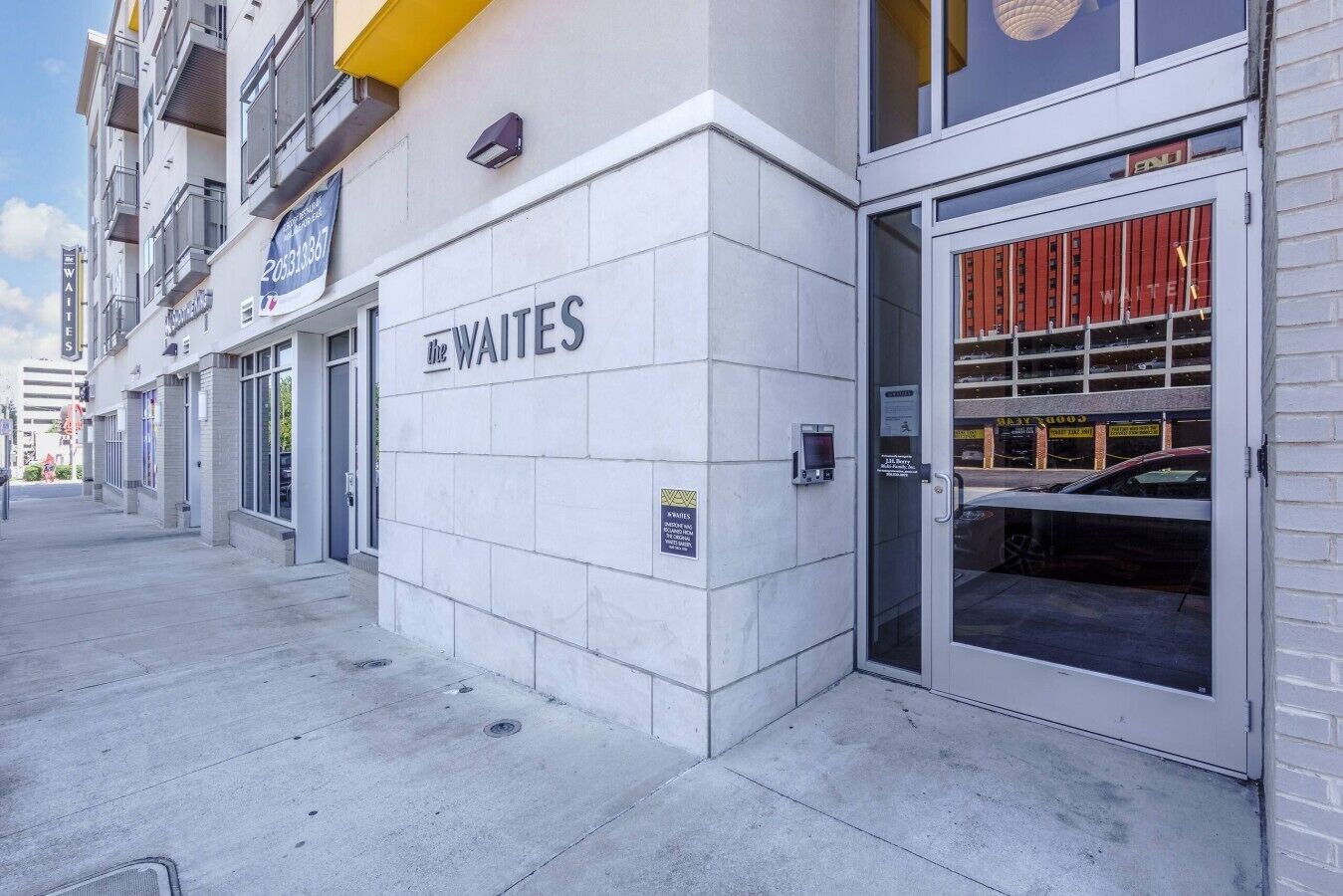 A building with a sign for 'The Waites' on the facade, a parking garage entrance, and a fire hydrant on the sidewalk.