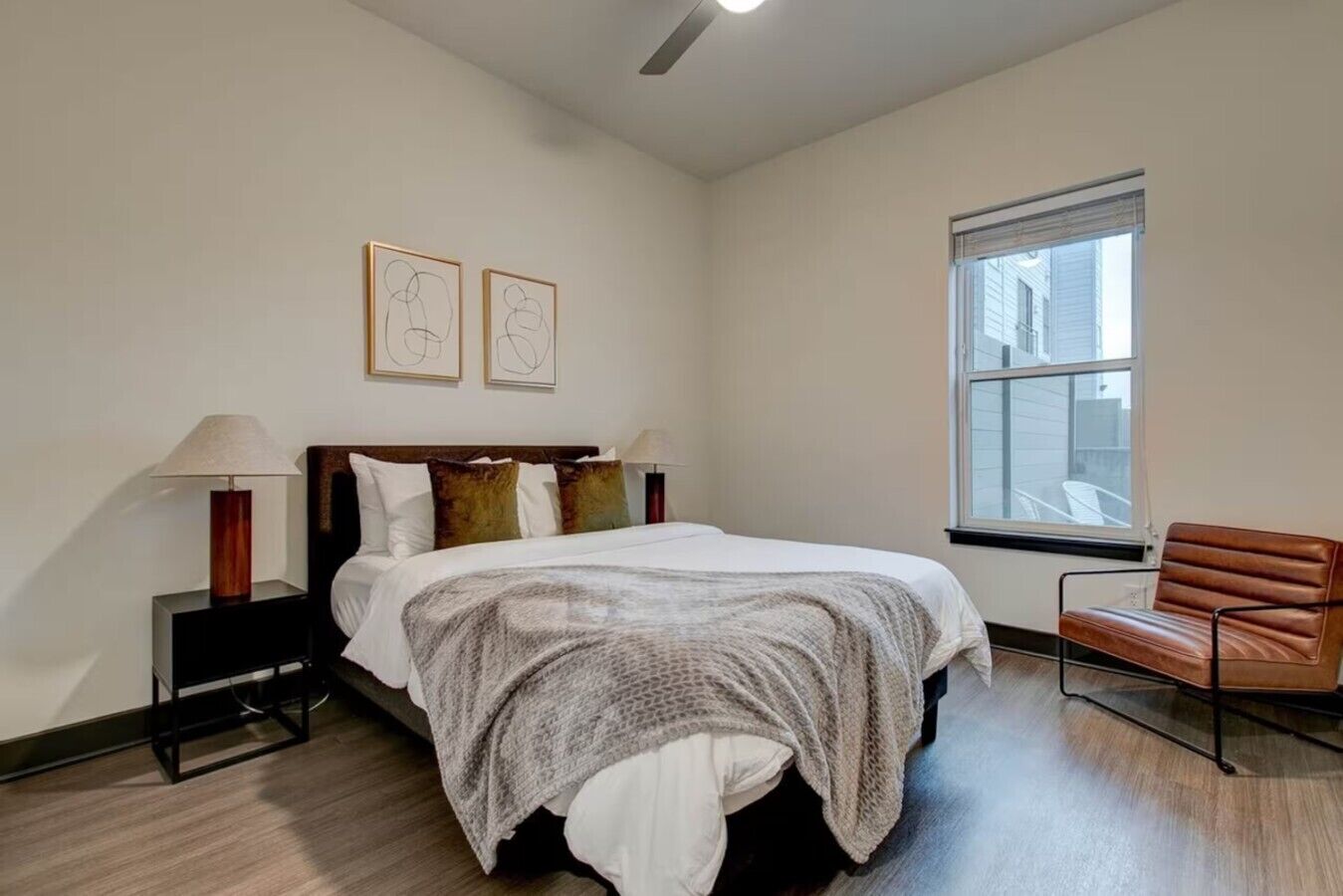 A bedroom with a bed, bedside lamps, a chair, and a window.