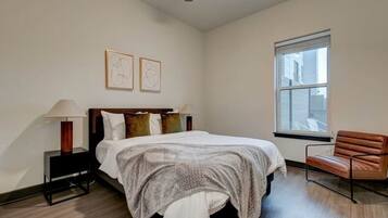 A bedroom with a bed, bedside lamps, a chair, and a window.