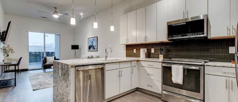 Cocina moderna con electrodomésticos de acero inoxidable, armarios blancos e iluminación colgante.