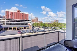 Blick vom Balkon auf einen Parkplatz mit einem Goodyear Reifenhandel, ein mehrstöckiges Gebäude mit roter Fassade und einem strahlend blauen Himmel.