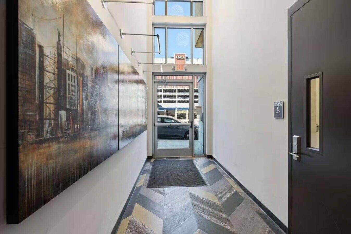A hallway with a large industrial-style mural, a glass door entrance, and a patterned floor.