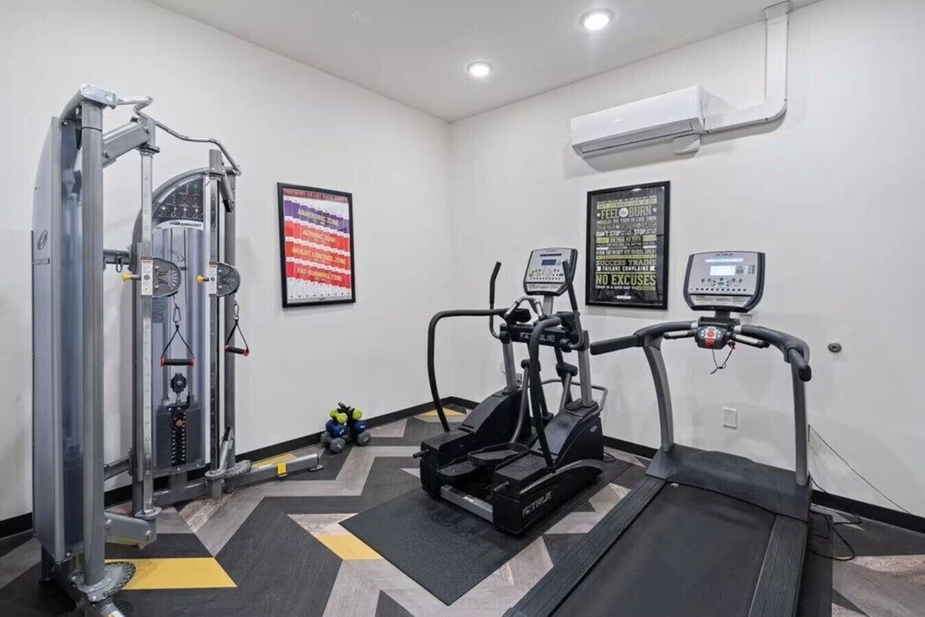 Ein Fitnessstudio mit Kraftgeräten, Laufbändern und einer Wandklimaanlage.