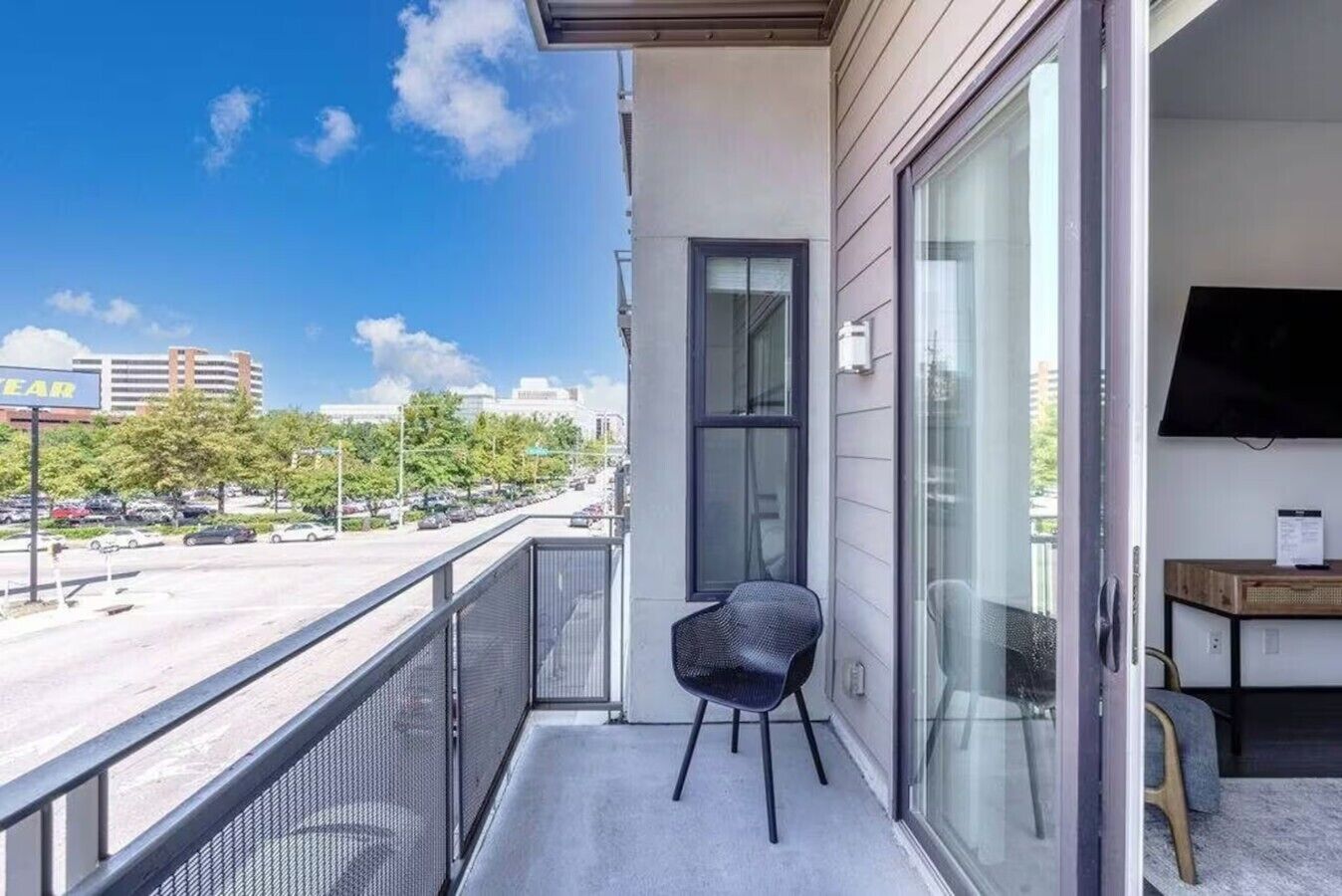 Een balkon met een stoel, een televisie en uitzicht op een parkeerplaats en gebouwen.