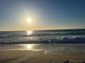 Une plage avec des vagues et le soleil qui se reflète sur l’eau.