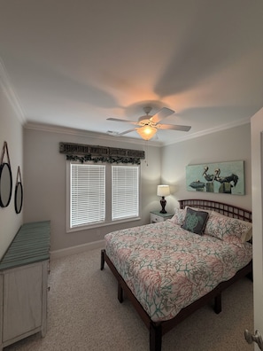 A bedroom with a bed, a ceiling fan, a window with blinds, a bedside table with a lamp, and a painting on the wall. - 6 BR Townhome in Carolina Beach with Public Beach Access across the Street! (Carolina Beach)