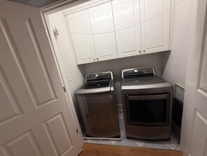 Une buanderie équipée de deux machines à laver et deux sèche-linge superposés, avec des placards blancs au-dessus et un plancher en bois.