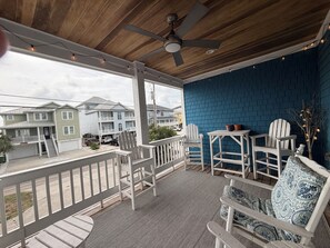 A covered porch with a ceiling fan, white chairs, a small table, and a blue brick wall. - 6 BR Townhome in Carolina Beach with Public Beach Access across the Street! (Carolina Beach)