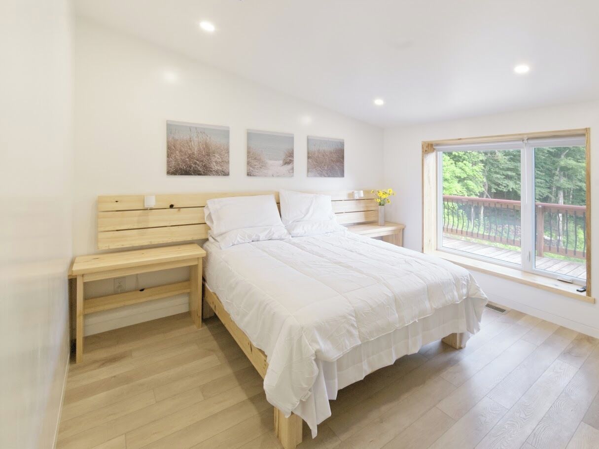 A bedroom with a bed, nightstands, a bench, and a window with a view of greenery.