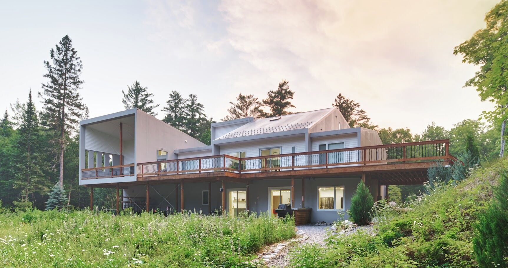 Une maison à deux étages avec un balcon, entourée de verdure et d’arbres.