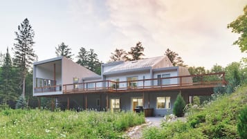 Une maison à deux étages avec un balcon, entourée de verdure et d’arbres.