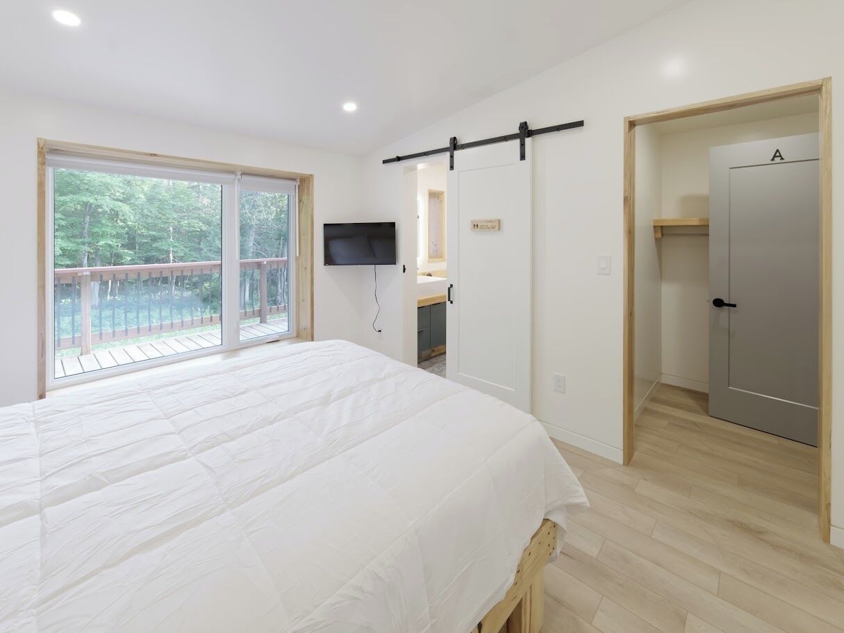 Een slaapkamer met een groot bed, een schuifdeur naar een balkon, een televisie, en een deur met de tekst 'A'.