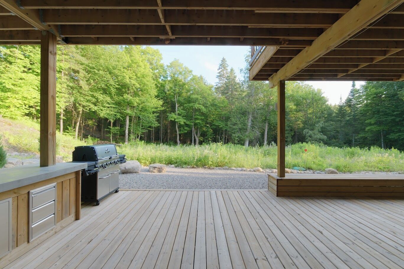 Une terrasse en bois dotée d’un barbecue et de rangements intégrés, entourée d’une zone boisée.