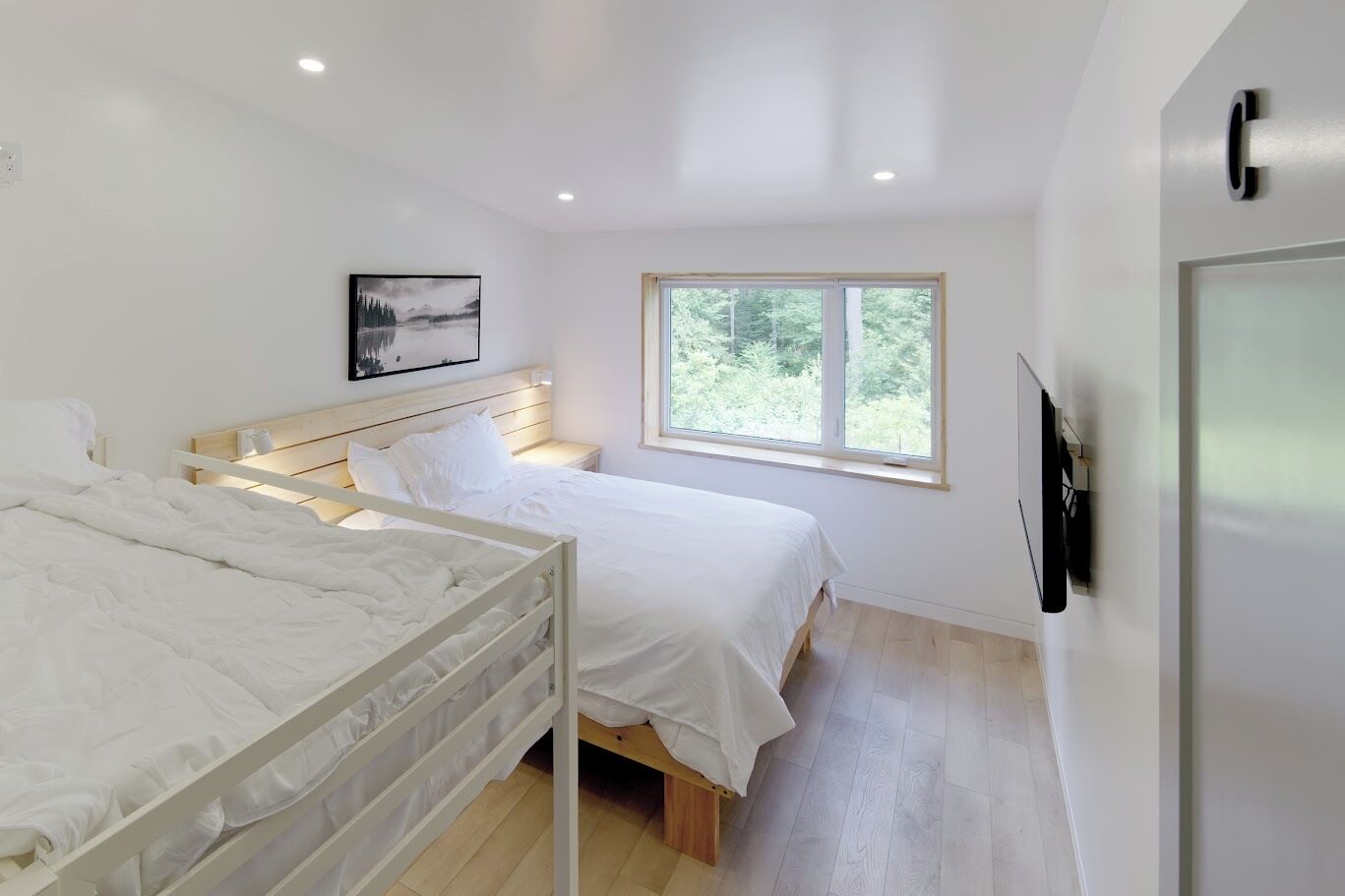 A bedroom with two beds, a window, a painting, and a TV on the wall.