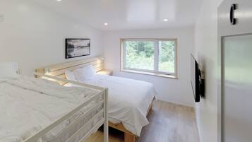 A bedroom with two beds, a window, a painting, and a TV on the wall.