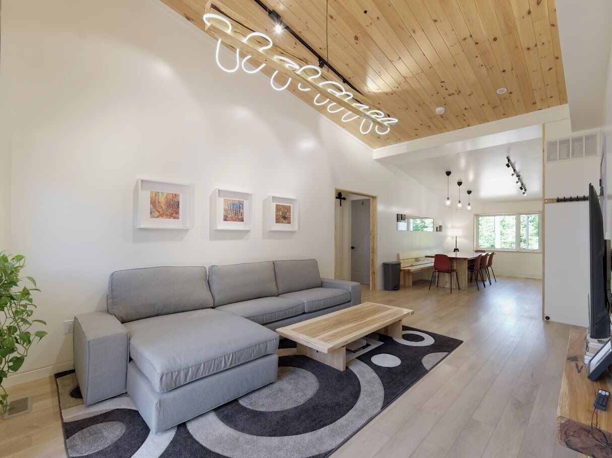 Un salon moderne avec un canapé gris, une table basse en bois et, au fond, un coin repas.