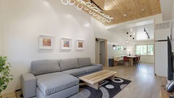 Un salon moderne avec un canapé gris, une table basse en bois et, au fond, un coin repas.