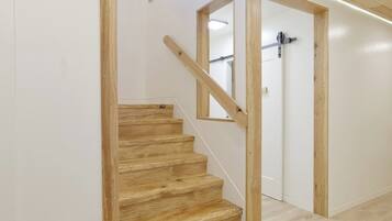 A wooden staircase with a handrail, white walls, and a door with a black handle.