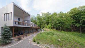 Ein modernes, zweistöckiges Haus mit überdachter Veranda, umgeben von einem bewaldeten Gebiet.