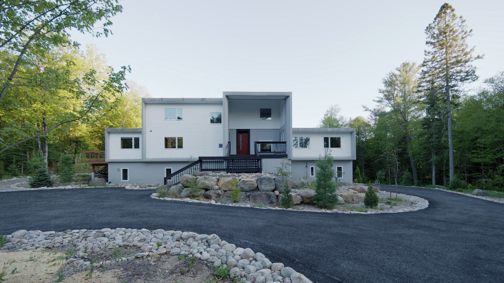 A modern two-story house with a central entrance, a covered porch, and a driveway leading to a gated entrance.