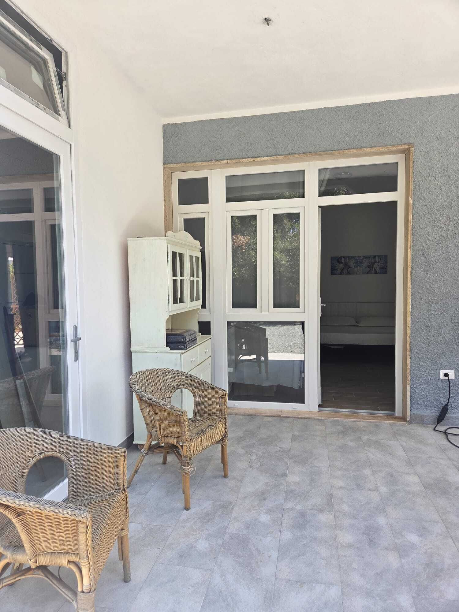 Une pièce dotée d’une grande porte-fenêtre coulissante donnant sur un balcon, de meubles en osier et d’une armoire blanche.