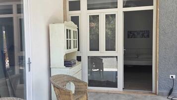 Une pièce dotée d’une grande porte-fenêtre coulissante donnant sur un balcon, de meubles en osier et d’une armoire blanche.
