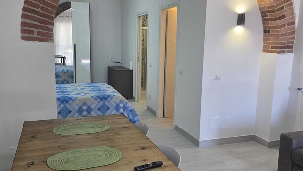 Ein modernes Zimmer mit einem Ziegelbogen, der zum Schlafbereich führt, ein Holztisch mit zwei grünen Unterlagen und einer Fernbedienung darauf.