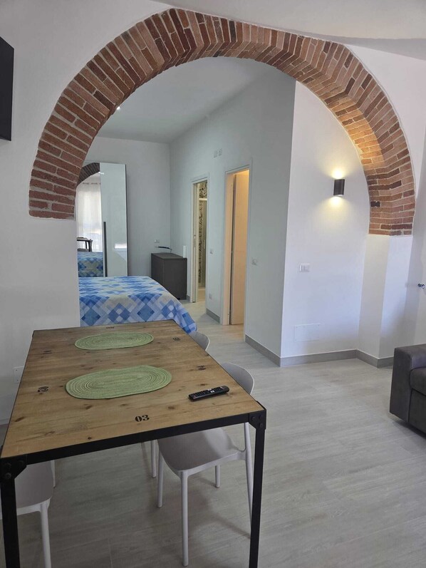 A modern room with a brick archway leading to a bedroom, a wooden table with two green placemats, and a remote control on it.