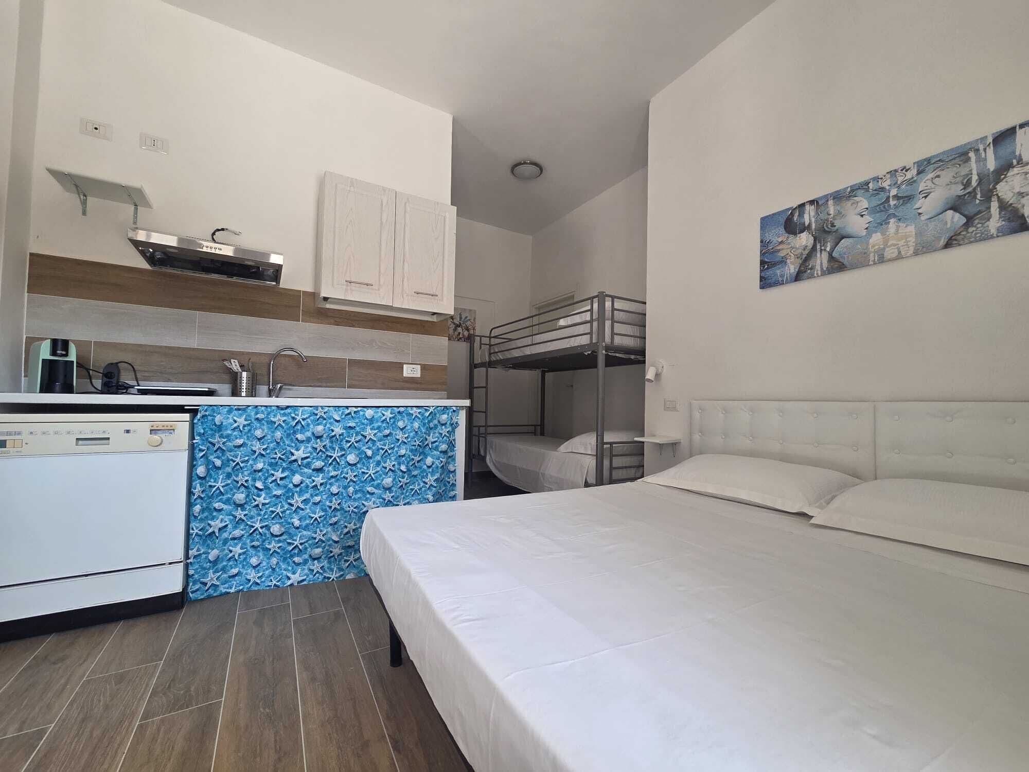 Une chambre d’hôtel compacte, dotée d’une kitchenette, d’un lit superposé et d’un tableau au mur.