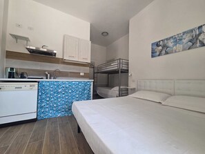 A compact hotel room with a kitchenette, a bunk bed, and a painting on the wall.