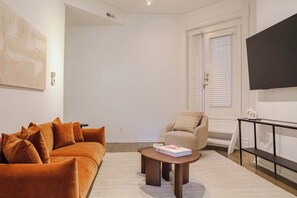 A living room with a sofa, armchair, coffee table, and a flat-screen TV mounted on the wall. - Designer Loft 3E | Heart of Gold Coast/River North (Chicago)