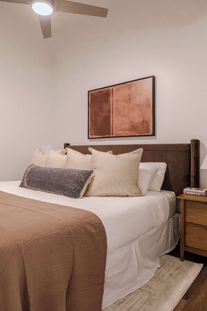 A neatly made bed with a brown headboard, a bedside table with a book, and a framed picture on the wall. - Designer Loft 3E | Heart of Gold Coast/River North (Chicago)