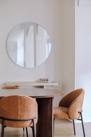 A dining area with a round table, two chairs, a mirror, and a small shelf with books. - Designer Loft 3E | Heart of Gold Coast/River North (Chicago)