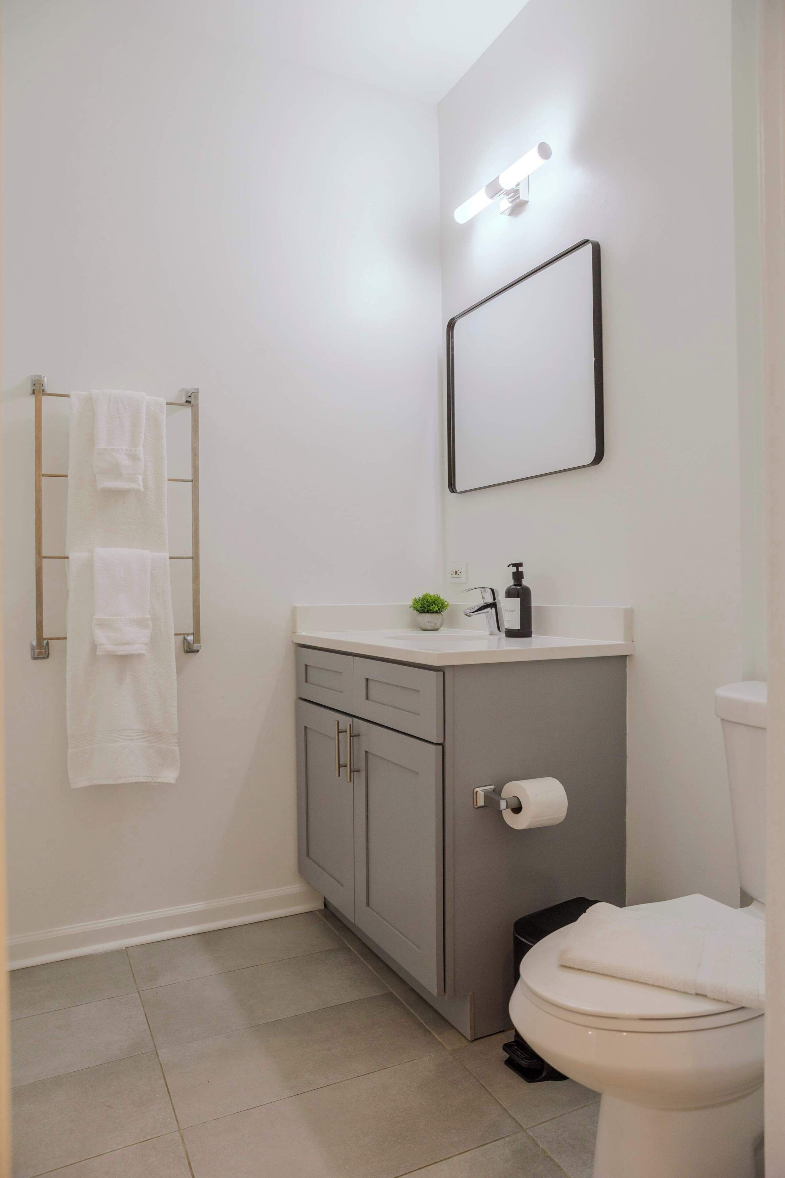 A bathroom with a toilet, a sink with a mirror above it, and a towel rack with two towels.