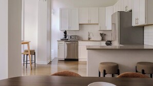 Eine moderne Küche mit weißen Schränken, einem Edelstahlkühlschrank und einem Holzespeisetisch mit vier Stühlen.