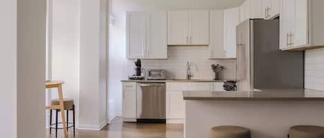 A modern kitchen with white cabinets, a stainless steel refrigerator, and a wooden dining table with four chairs.