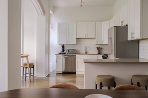 A modern kitchen with white cabinets, a stainless steel refrigerator, and a wooden dining table with four chairs. - Designer Loft 3E | Heart of Gold Coast/River North (Chicago)
